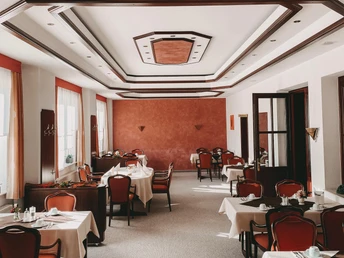 Ein eleganter Speiseraum mit roten Stühlen und weißen Tischdecken, umgeben von großen Fenstern.