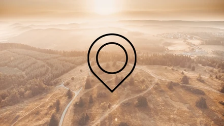 Drohnenaufnahme einer weitläufigen Landschaft mit Bergen, Wiesen und Wäldern mit der Zeichnung eines Markierungszeichens im Vordergrund. Dieses Bild dient als Symbolbild für Sehenswürdigkeiten.