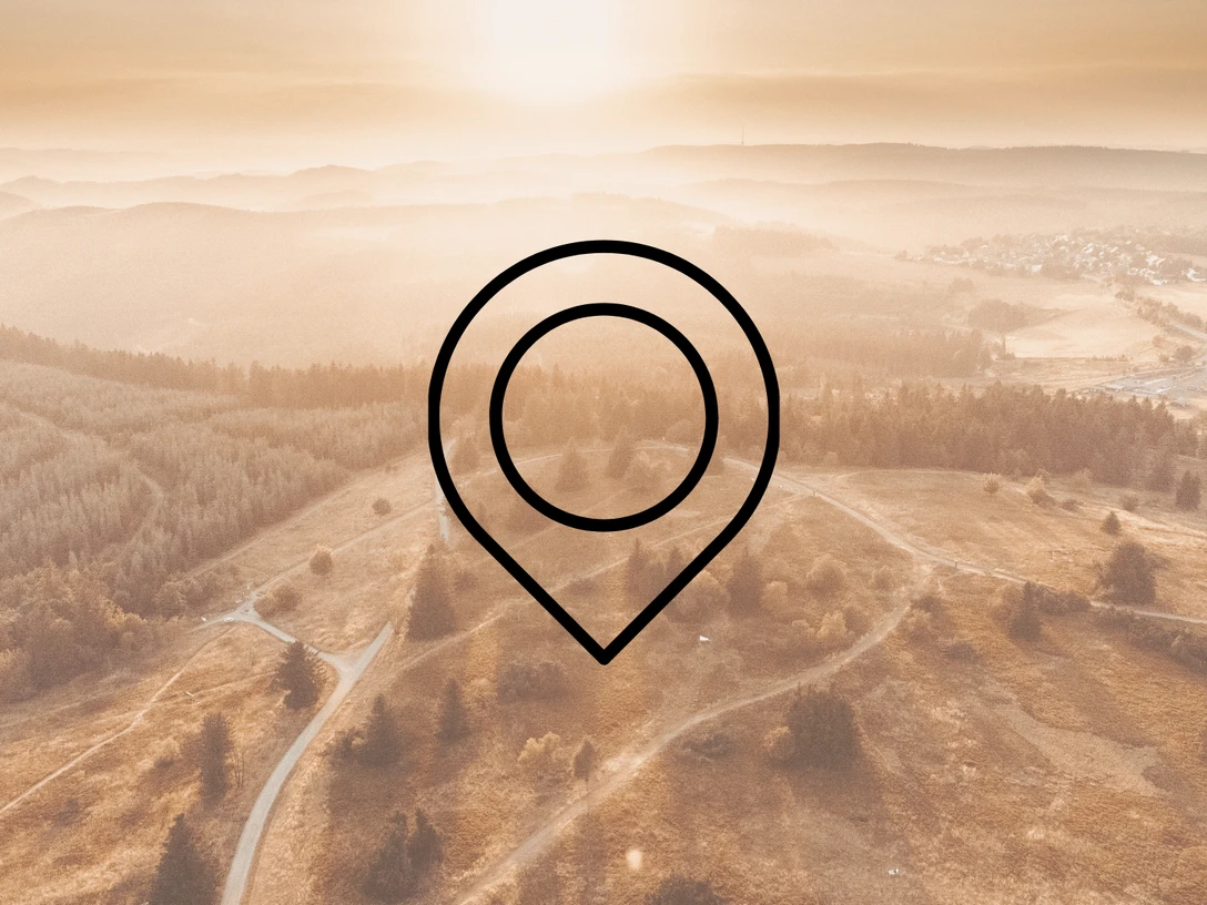 Eine Drohnenaufnahme von einer weiten Landschaft mit Wäldern, Wiesen und Bergen mit der Zeichnung eines Markierungszeichens im Vordergrund. Dieses Bild dient als Symbolbild für Sehenswürdigkeiten.
