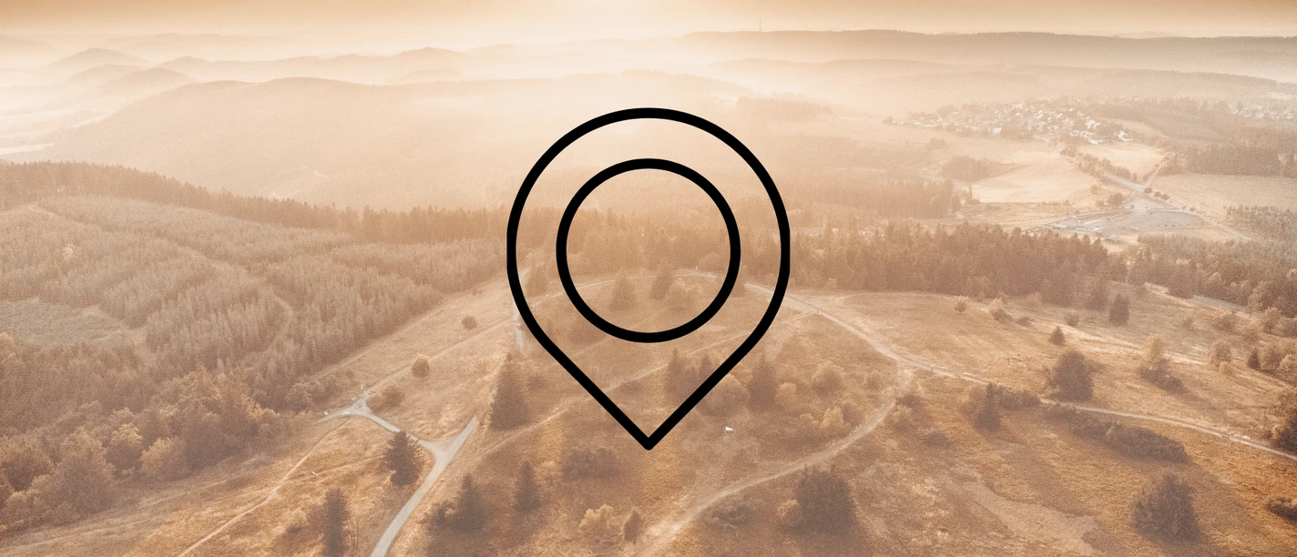 Eine Drohnenaufnahme von einer weiten Landschaft mit Wäldern, Wiesen und Bergen mit der Zeichnung eines Markierungszeichens im Vordergrund. Dieses Bild dient als Symbolbild für Sehenswürdigkeiten.