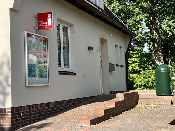 Tourist-Information Außenansicht Eingang der Tourist-Information Rastede mit rotem i-Schild am hellen Gebäude.