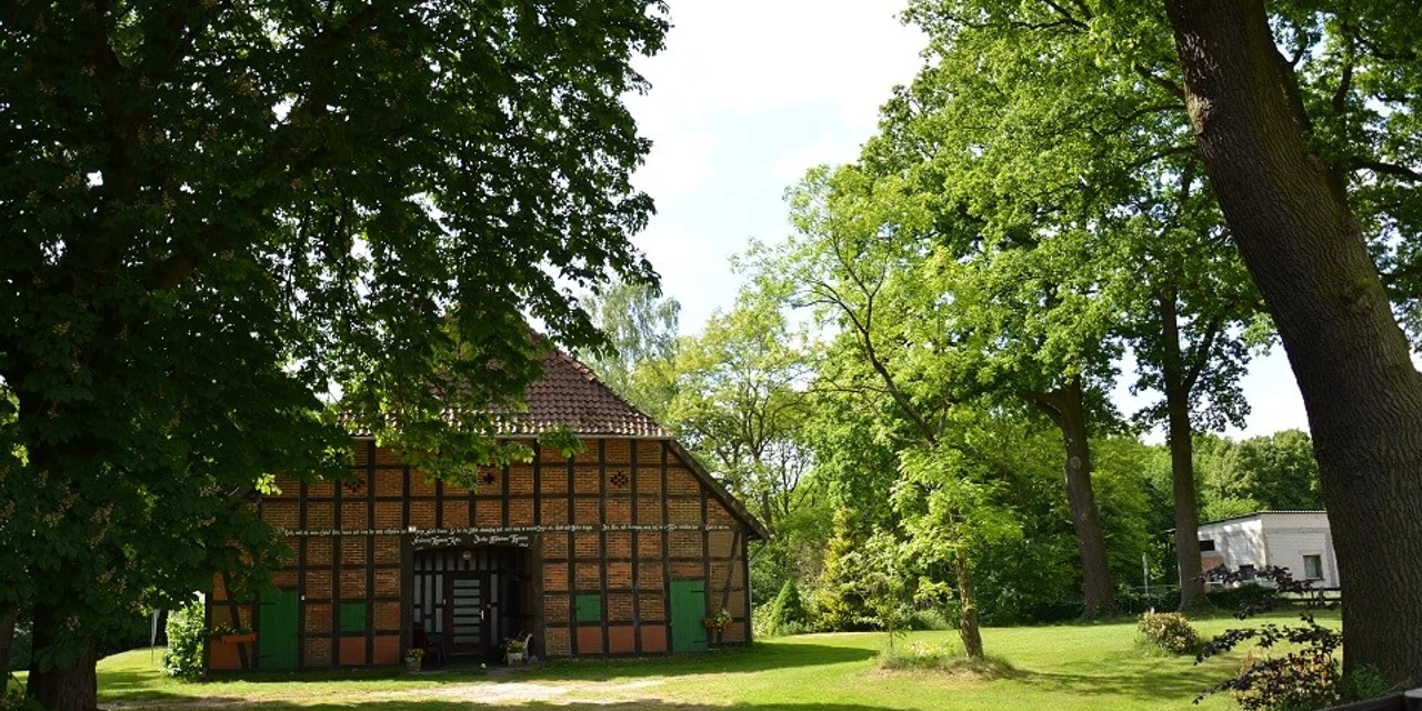 bevensen-fachwerkhaus-klein Ein traditionelles niedersächsisches Fachwerkhaus steht inmitten einer grünen Landschaft voller Bäume.