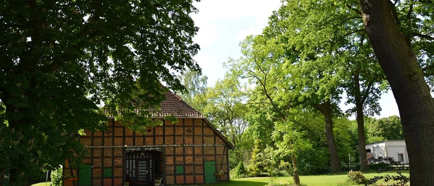 bevensen-fachwerkhaus-klein Ein traditionelles niedersächsisches Fachwerkhaus steht inmitten einer grünen Landschaft voller Bäume.