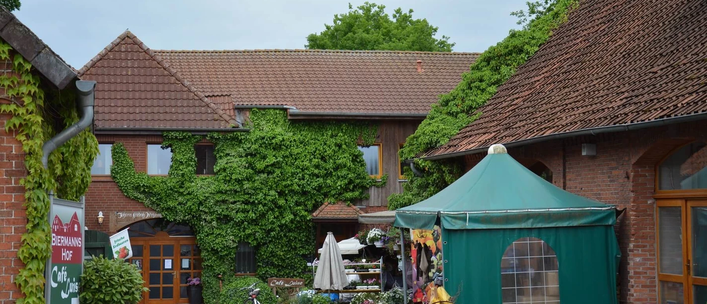 eilvese Ein Hof mit Ziegelgebäuden und grünem Bewuchs, ein Verkaufsstand mit Pflanzen und Dekorationen.