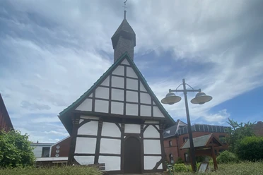 St. Laurentius-Kapelle Nammen Fachwerk-Kapelle mit spitzem Turmdach in Porta Westfalica, umgeben von Büschen und Nachbarhäusern.