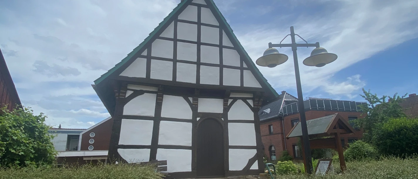 St. Laurentius-Kapelle Nammen Fachwerk-Kapelle mit spitzem Turmdach in Porta Westfalica, umgeben von Büschen und Nachbarhäusern.