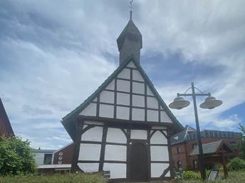 St. Laurentius-Kapelle Nammen Fachwerk-Kapelle mit spitzem Turmdach in Porta Westfalica, umgeben von Büschen und Nachbarhäusern.