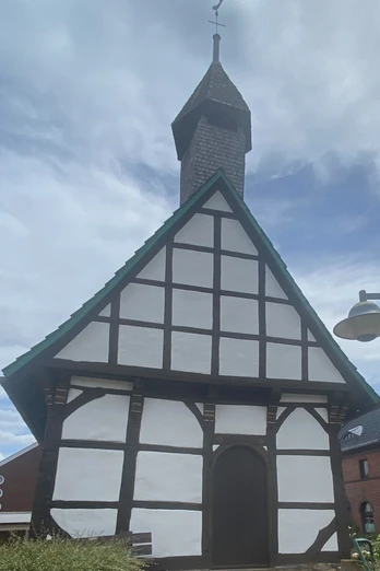 St. Laurentius-Kapelle Nammen Fachwerk-Kapelle mit spitzem Turmdach in Porta Westfalica, umgeben von Büschen und Nachbarhäusern.