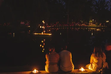 Kerzenlichter spiegeln sich nachts im See, Besucher sitzen am Ufer im Kurpark