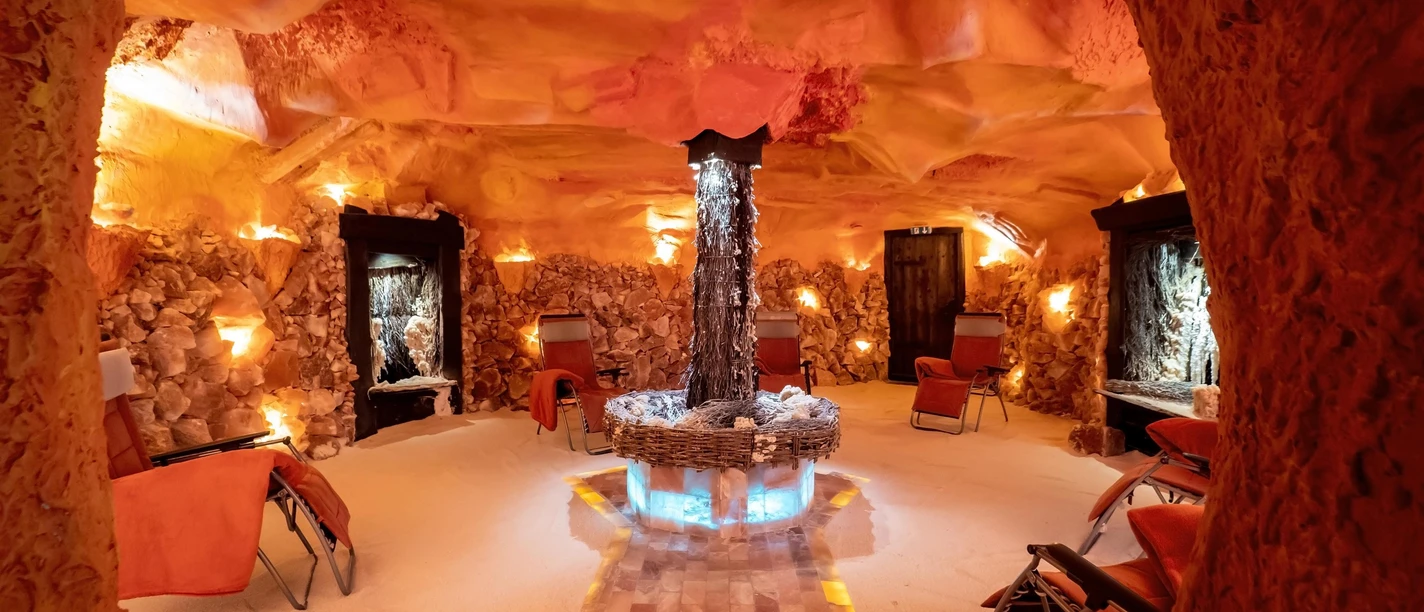 Warm beleuchtete Salzgrotte mit Liegestühlen, Salzwänden und leuchtendem Brunnen