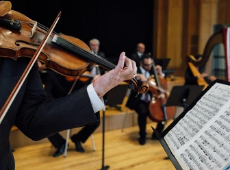 Staatsbad Salzuflen_Orchester_Geige Notenblatt Ein Violinenspieler spielt in einem Orchester. Im Hintergrund sind weitere Musiker zu sehen.