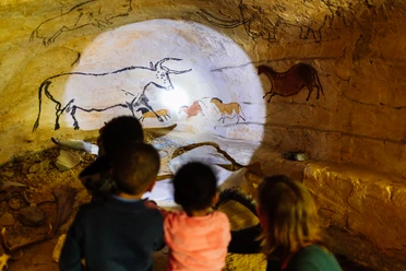 Steinzeitlicht und Höhlenblick Kinder betrachten fasziniert Höhlenmalereien mit Tieren in einer beleuchteten Höhle aus der Steinzeit.