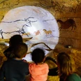 Steinzeitlicht und Höhlenblick Kinder betrachten fasziniert Höhlenmalereien mit Tieren in einer beleuchteten Höhle aus der Steinzeit.
