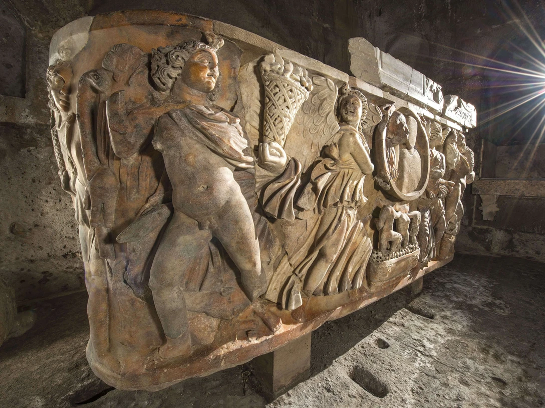 Römischer Sarkophag im Römergrab Köln Weiden Antiker Sarkophag mit kunstvollen Reliefs von Figuren und Szenen in einem steinernen Gewölbe.Ancient sarcophagus with artistic reliefs of figures and scenes in a stone vault.