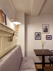 Münte1.jpg Gemütliche Café-Ecke mit grauer Sitzbank, Holztisch, gelber Blume und gerahmten Bildern an der Wand.