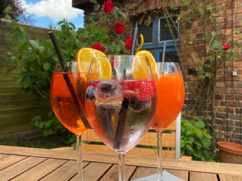 Münte3.jpg Drei volle Weingläser mit Aperitifs, dekoriert mit Zitrus- und Beerenfrüchten, auf einem Holztisch.