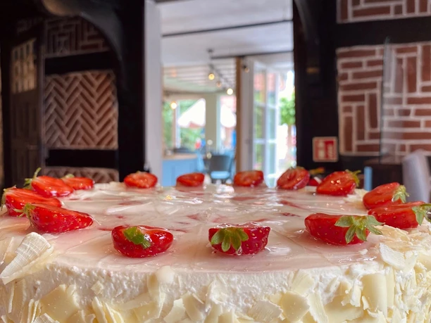 Münte4.jpg Ein cremiger Kuchen mit weißen Schokoraspeln und leuchtend roten Erdbeeren auf einem Holztisch.