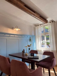 Münte8.jpg Ein gemütlicher Café-Tisch mit vier rosa Stühlen in einem hellen Raum mit Fenster und dekorativer Wand.