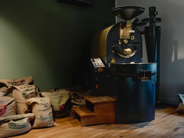 EOS2.jpg Industrieller Kaffeeröster in einem Raum mit Jutesäcken voll Kaffeebohnen auf Holzboden.