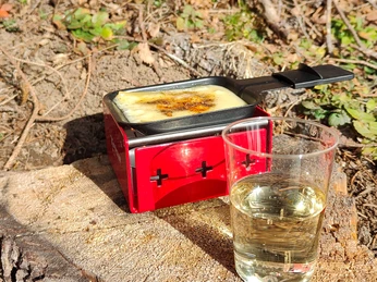 Arrêt raclette lors de la randonnée en raquettes à neige Raclette-Öfelchen mit Käse und ein Glas Wein davorRaclette cubes with cheese and a glass of wine in front of itPetits cubes de raclette avec du fromage et un verre de vin devant