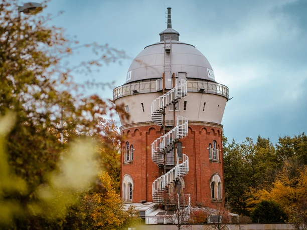Camera Obscura, Mülheim an der Ruhr <p>Roter Wasserturm mit Wendeltreppe, eingebettet in herbstliche Bäume vor bewölktem Himmel.</p>