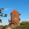 Landschaftsfenster Tange.jpg Das Bild zeigt einen Backsteinturm mit einem spitzen, roten Ziegeldach. Der Turm ist mit hölzernen Treppen und Geländern umgeben, die Besucher zur Aussichtsplattform führen. Links im Vordergrund steht ein großer Baum, und im Hintergrund erstreckt sich die Landschaft unter einem klaren blauen Himmel. Der Turm befindet sich in einer grünen Umgebung, die auf die ländliche Idylle der Region hindeutet.