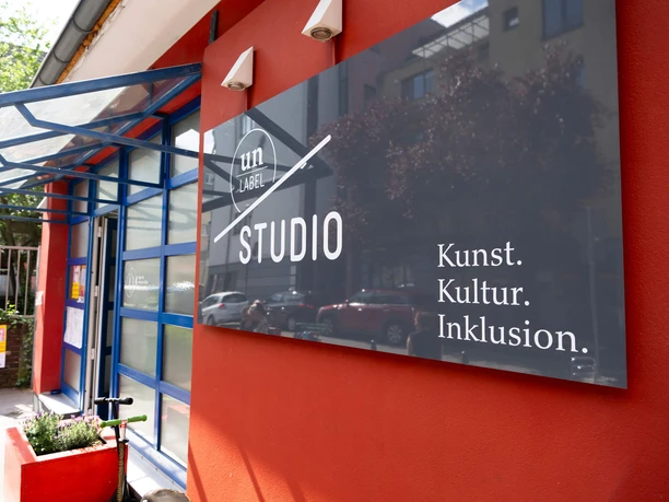 Un-Label Auf dem Bild ist das un-Label Studio in Ehrenfeld zu sehen. Ein großes Schild weist auf Kunst, Kultur und Inklusion hin.