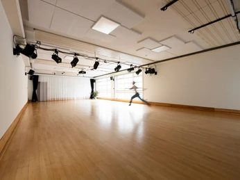 Un-Label Ein großzügiger, lichtdurchfluteter Tanzraum mit Holzfußboden. Eine Person tanzt dynamisch im Raum.A spacious, light-flooded dance room with a wooden floor. One person dances dynamically in the room.