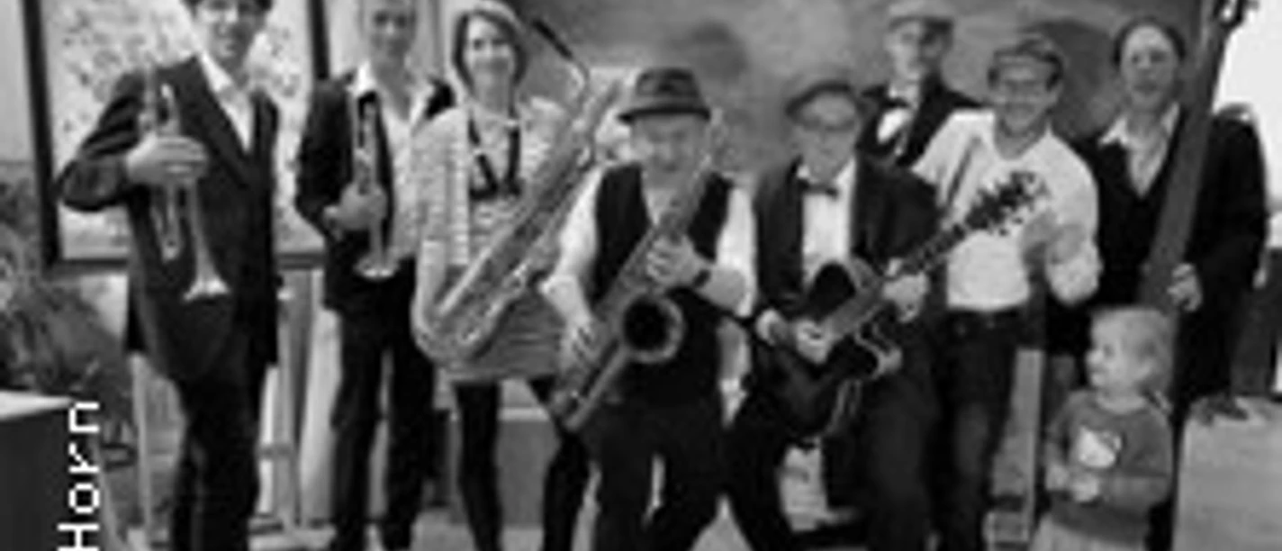 Eine Gruppe von acht Musiker*innen und einem Kind posieren lachend mit Instrumenten wie Saxophon und Gitarre.