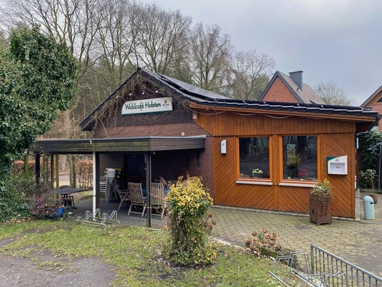 Backsteingebäude mit Holzfassade, überdachter Terrasse und grüner Umgebung im Waldgebiet.
