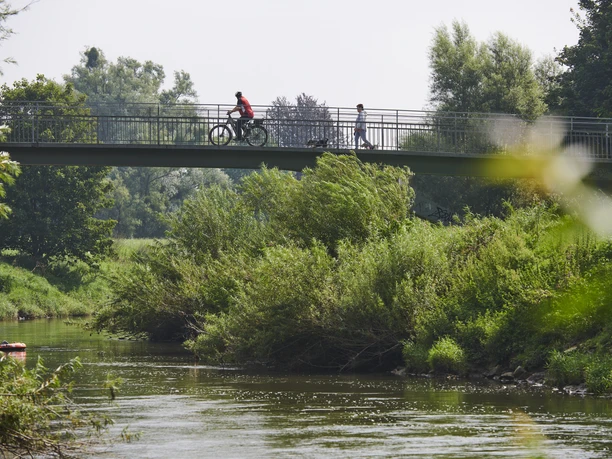 Brücke Sielpark Eine Metallbrücke überspannt einen ruhigen Fluss, während Bäume und Büsche die Umgebung säumen.