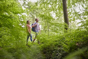 Wandern Zwei Personen wandern auf einem Waldpfad, umgeben von dichtem Grün und hohen Bäumen.