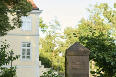 Wasserschluss Ovelgönne (c) Peter Hübbe Das Foto zeigt einen Stein mit der Inschrift "Wasserschloss Ovelgönne" vor einem historischen Gebäude.