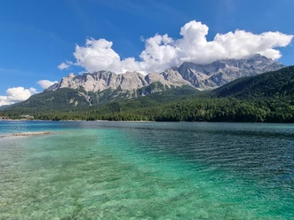 Klares türkisfarbenes Wasser vor bewaldeten Ufern und markanten Bergen unter blauem Himmel