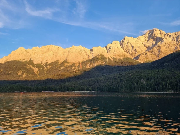 Sonnenuntergang am Eibsee Bergkette im warmen Abendlicht spiegelt sich auf dem ruhigen Wasser eines klaren Sees
