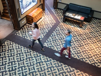 Herford-Daniel-Poeppelmann-Haus-Teutoburger-Wald-Tourismus-M-Schoberer (3).jpg Zwei Personen gehen auf einem kunstvoll gemusterten Boden in einem historischen Gebäude.