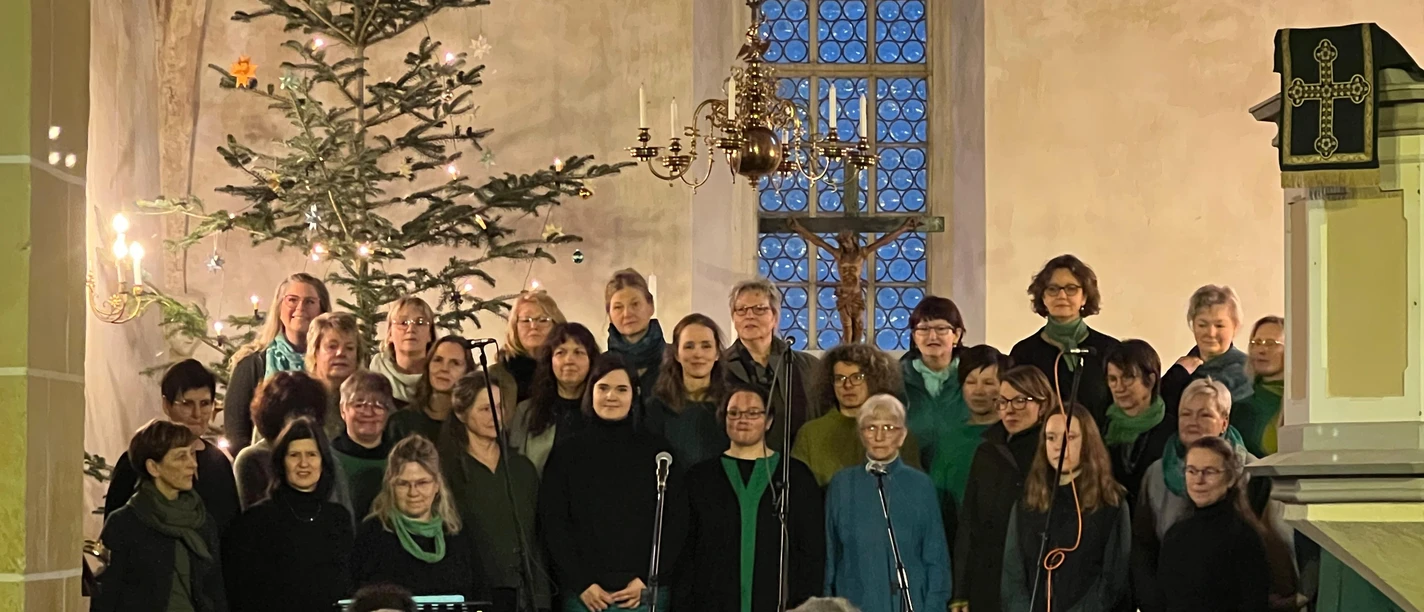 Melodiven Weihnachtskonzert Ein Chor von Erwachsenen singt vor glanzvoll geschmücktem Weihnachtsbaum in einer Kirche.