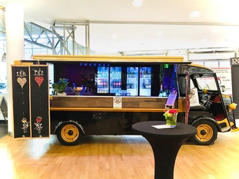 BarcarrosseIndoor4_3.jpg Ein moderner, dreirädriger Oldtimer Imbisswagen mit Holzverkleidung. Im Hintergrund Kühlschränke mit Getränken.A modern, three-wheeled vintage food truck with wooden paneling. Refrigerators with drinks in the background.