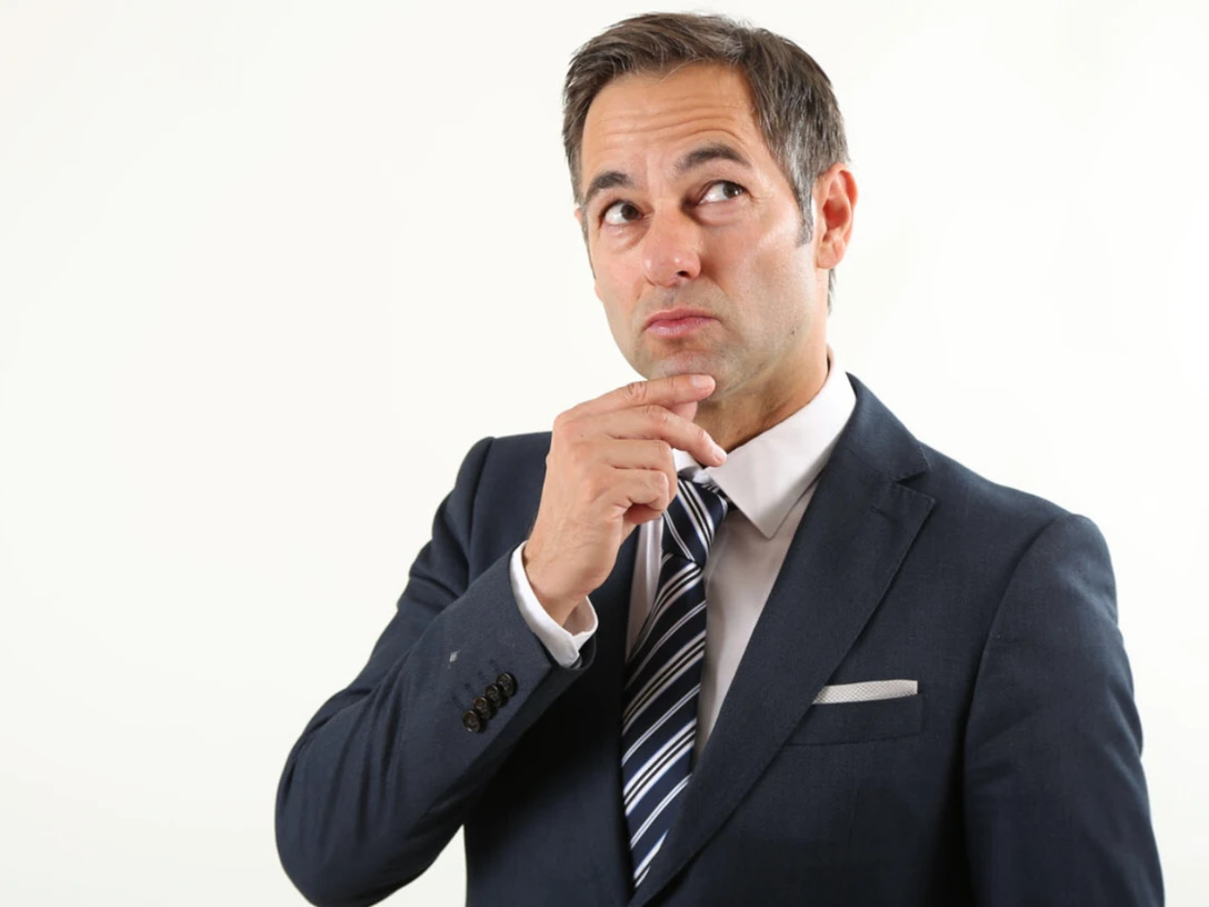 thieß-neubert.png Mann in Anzug mit nachdenklichem Blick, hält eine Hand ans Kinn vor hellem Hintergrund.