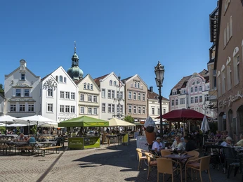 Gänsemarkt-Hoekerfest2019-Pro Herford GmbH.jpg Eine belebte Einkaufsstraße in Herford mit Menschen, die Cafés genießen, unter blauem Himmel.