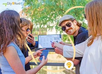 Herford-CityHunt-CityHunters GmbH & Co.KG_1..jpg Vier Personen halten Hinweise und Smartphones, konzentriert auf eine Stadtrallye an einem sonnigen Tag.