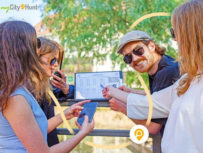 Herford-CityHunt-CityHunters GmbH & Co.KG_1..jpg Vier Personen halten Hinweise und Smartphones, konzentriert auf eine Stadtrallye an einem sonnigen Tag.