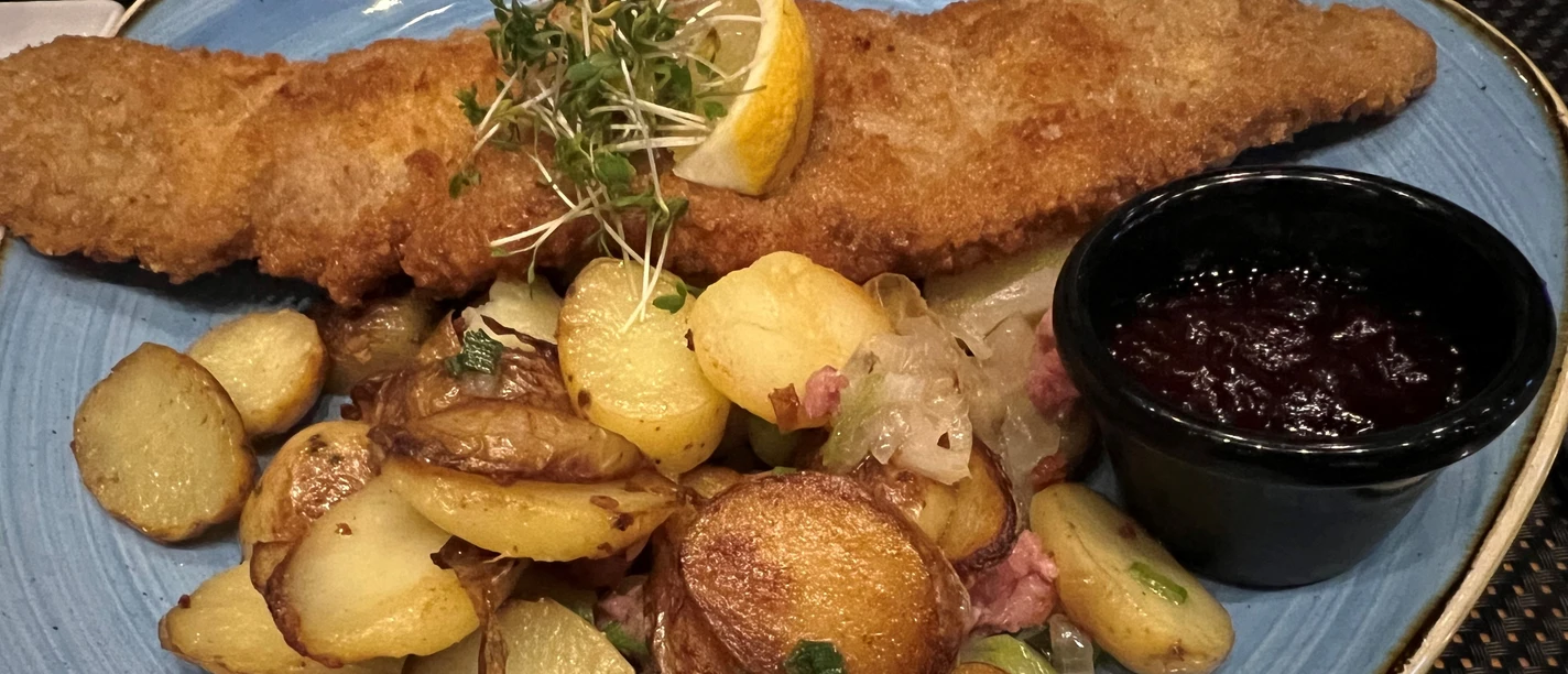 A crispy Wiener schnitzel accompanied by golden brown fried potatoes and cranberries.
