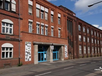 raum13 Das Bild zeigt einen Backsteinbau mit blauer Eingangstür und großflächigen Fenstern.The picture shows a brick building with a blue entrance door and large windows.