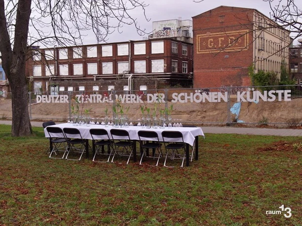 raum13 Eine lange, festlich gedeckte Tafel steht unter freiem Himmel vor einer alten Backsteinfabrik.