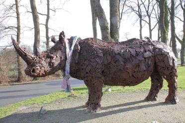 Nashorn-Spohle2-DerWiefelsteder.jpeg Eine beeindruckende Nashorn-Skulptur aus Metallteilen steht im Freien, umgeben von kahlen Bäumen.