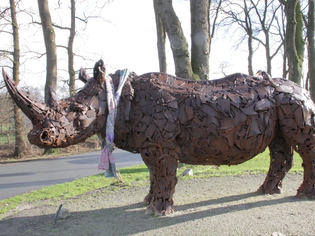 Nashorn-Spohle2-DerWiefelsteder.jpeg Eine beeindruckende Nashorn-Skulptur aus Metallteilen steht im Freien, umgeben von kahlen Bäumen.