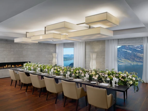 Festlich gedeckter Speisetisch mit Blumen, Kamin und Blick auf See und Berge