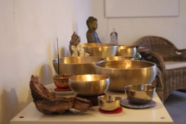 AusKlang am Abend.jpg Mehrere goldene Klangschalen mit Räucherstäbchen in einem stillen Raum mit Meditationsfigur.