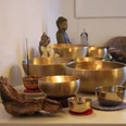 AusKlang am Abend.jpg Mehrere goldene Klangschalen mit Räucherstäbchen in einem stillen Raum mit Meditationsfigur.